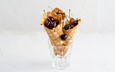 Three ice cream cones filled with cherries in a glass beaker on a light white concrete background.