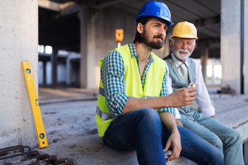 Happy mature and young engineer, architect, worker sitting at building site and resting