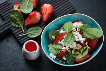 Salad with fresh strawberry, baby spinach, cottage cheese and peanuts, horizontal shot over black stone surface