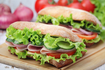 Two sandwiches with fresh vegetables, ham and cheese in ciabatta bread