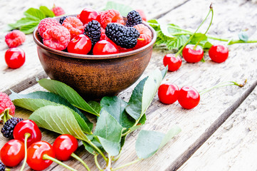 juicy fresh delicious berries raspberries, cherries, mulberries in a bowl on wooden background.