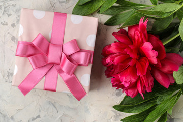 Beautiful bright pink flowers of peonies and a gift box on a bright concrete background. top view.