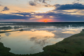 Forest lake in the morning fog, in the rays of the dawn sun. Drone view.