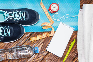 Naklejka na ściany i meble Healthy lifestyle and sports background. Sports shoes, Notepad and pen, stopwatch and water bottle on wooden background with copyspace, top view.