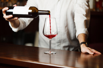 Male sommelier pouring red wine into long-stemmed wineglasses.