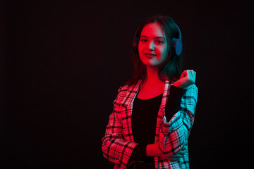 Cheerful young girl wearing heaphones and smiling to the camera in studio with colored lighting