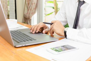 Businessman working on laptop with paperwork on table.
