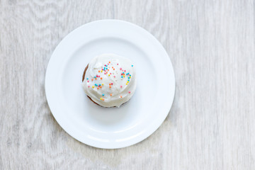 Tasty cupcake in the plate on a white wooden table. Sweet beautiful cake for birthday greeting card or party invitation
