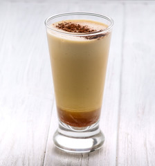 Frothy, layered cappuccino in a clear glass mug with cinnamon sprinkled on top