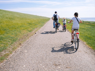 Back view cyclists family traveling on the road in the dune area of Schiermonnikoog island. Active family sport. Summer travel and vacation concept