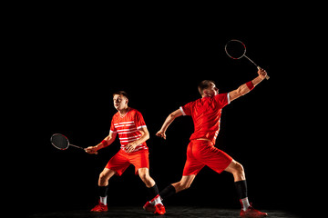 Naklejka na ściany i meble Young man playing badminton isolated on black background in mixed light. Male model in sportwear and sneakers with the racket in action, motion in game. Concept of sport, movement, healthy lifestyle.