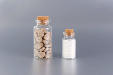 natural medicine bottles with herbal pills and globules on gray background