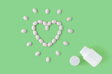 Pills in shape of heart dropped from bottle on green background. Flat lay, top view.