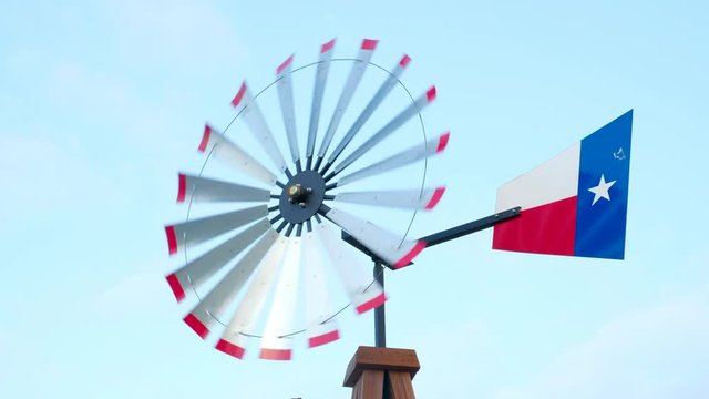 Moving windmill used for water aeration with painted Texas flag on blue sky background
