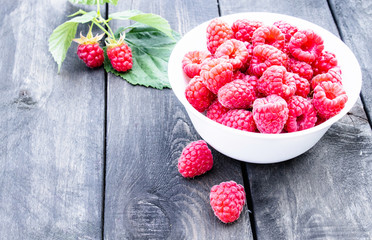 Ripe red raspberries on a bowl on the background of the old dark boards. Selective focus.