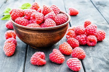 Ripe red raspberries on a bowl on the background of the old dark boards. Selective focus.
