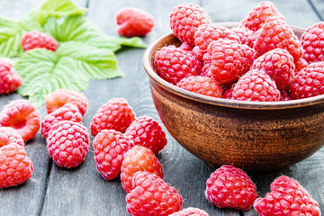 Ripe red raspberries on a bowl on the background of the old dark boards. Selective focus.