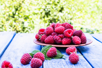 Ripe red raspberries on a bowl against the background of blue boards. Selective focus.