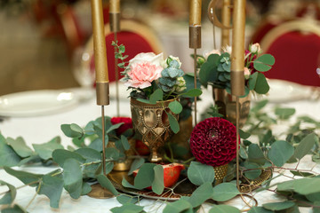 The wedding table setting is decorated with fresh flowers in a brass bowl and golden candles in brass candlesticks. Wedding floristry. Banquet table for guests. Bouquet with dahlias and eucalyptus