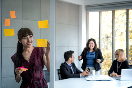 business woman intend at write paper note at glass board and business people discuss marketing plan background