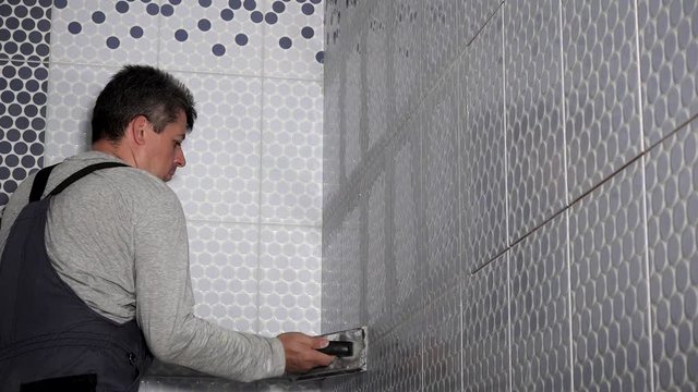 Worker putting fugue on wall tiles joints in bathroom. Man grouting tiles