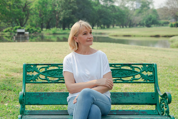 Lonely elderly woman sitting on a bench in a city park background