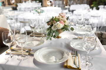 Fototapeta premium Wedding table setting decorated with fresh flowers in a brass vase. Wedding floristry. Banquet table for guests outdoors with a view of green nature. Bouquet with roses, eustoma and eucalyptus leaves