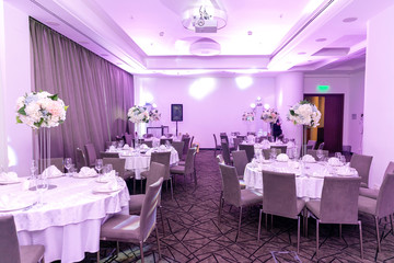 Beautiful table setting with crockery and white flower arrangements in a vase on a high stem for a party, wedding reception or other festive event. Glassware and cutlery for catered event dinner