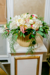 A white bouquet of peonies, hortensia and anthurium in a gold flowerpot on a white pillar in a classic style