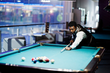 Young handsome african man wearing white shirt, black vest and bow tie play pool billiard.