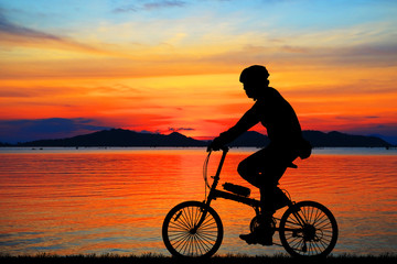 Obraz premium Silhouette man and bike relaxing on blurry sunrise sky background.