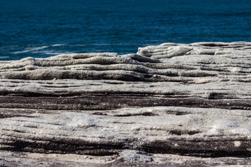 Oceanside rocky cliff top sandstone wave ridges with blue coastal sea in background