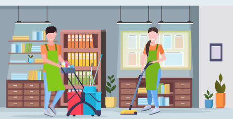 man pushing trolley cart with cleaning supplies woman using vacuum cleaner couple cleaners in uniform working together modern co-working center office interior flat full length horizontal