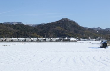 積雪の畑から見た民家と山の様子です