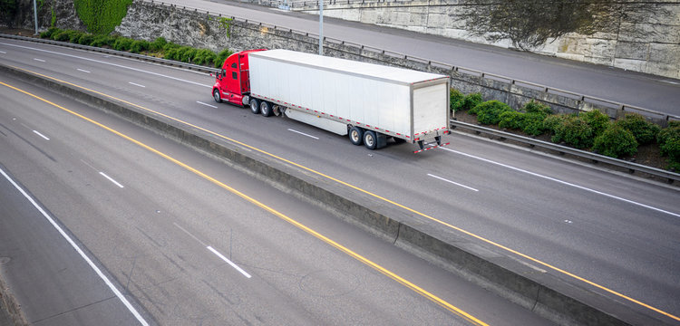 Red Big Rig Long Haul Semi Truck With Dry Van Semi Trailer Running On Divided Wide Highway