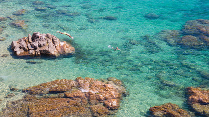 An upper view of the rocks at seashore with a diving man and a swimming woman.