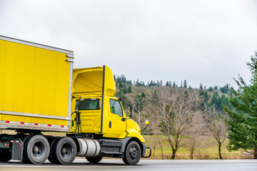 Fototapeta na wymiar Yellow big rig day cab semi truck for local deliveries transporting yellow dry van semi trailer on the road with trees on the side