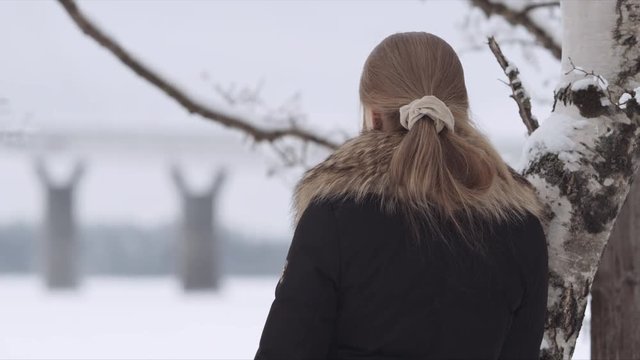 Medium Shot of a blonde woman waiting near a tree someone while looking at Replot Bridge in the distance. Vaasa (Finland) 
Shot on Red Monster 8K. In 4K