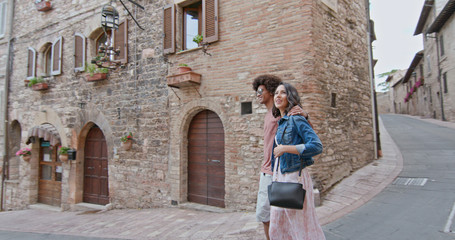 Fototapeta na wymiar Romantic couple walking visiting rural town of Assisi.Side follow. Friends italian trip in Umbria.4k slow motion