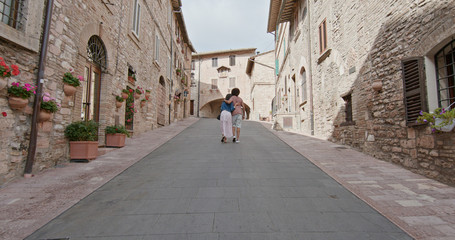 Fototapeta na wymiar Romantic couple walking visiting rural town of Assisi.Back follow.Friends italian trip in Umbria.4k slow motion