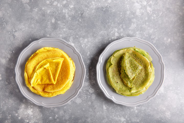 Yellow and green pancakes on gray plate.  Stack of spinach crepes and crepes tinted turmeric on concrete background. Top view, copy space.