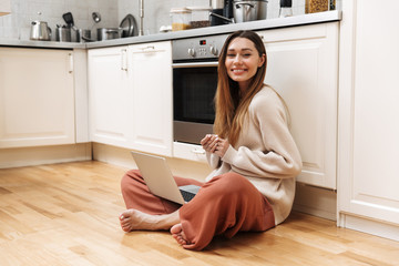 Cheerful young girl sitting on a floor at the kitchen