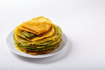 Yellow and green pancakes on white plate.  Stack of spinach crepes and crepes tinted turmeric on white background.