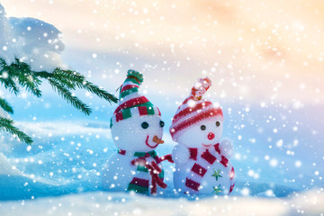 Two small funny toys baby snowman in knitted hats and scarves in deep snow outdoors on bright blue and white copy space background. Happy New Year and Merry Christmas greeting card.