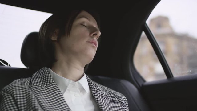 woman with brown hair in white blouse and check coat riding in car and just sleeping