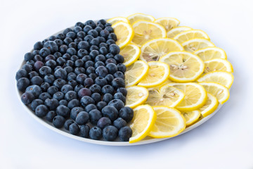 Blueberry berries and lemon slices on a round plate on a white background. Top angle view. Geometric view of berries and fruits on a plate.