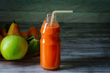 Fresh juice from orange green apple with pears and carrots in a bottle with a straw front view on wooden background