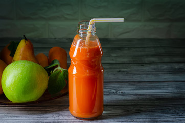 Fresh juice from orange green apple with pears and carrots in a bottle with a straw front view on wooden background