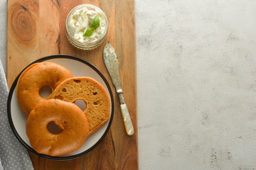 Delicious bagels with cream cheese on wooden board, pastry bread for breakfast. Top view. Copy space.