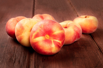 A closeup photo of vibrant organic flat saturn peaches on a dark rustic wooden background